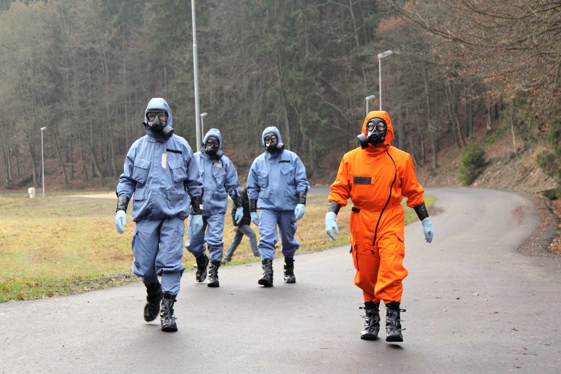 Four people walking in safety suits and gasmasks